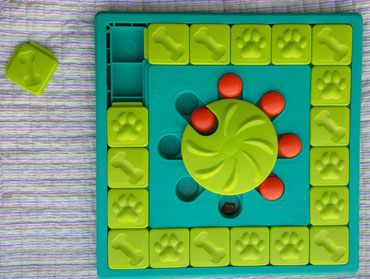 Outward Hound Multi Puzzle Interactive Treat Puzzle with tile pulled out and orange caps under the wheel